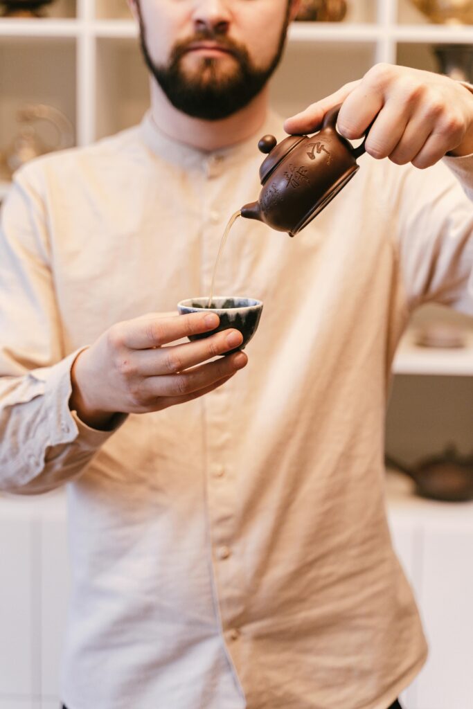Man pouring tea from a small teapot into a cup during a Japanese tea ceremony.