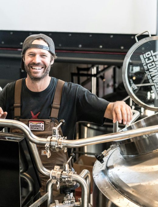 Happy brewer in a craft brewery standing near stainless steel equipment.