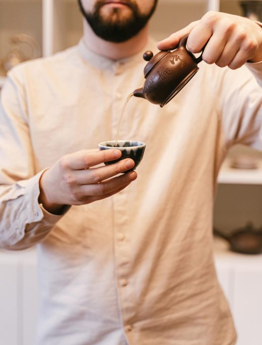 Man pouring tea from a small teapot into a cup during a Japanese tea ceremony.